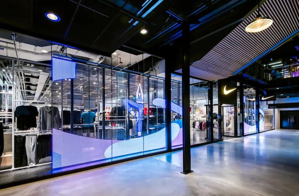 Прозрачные экраны с фиолетовой графикой вдоль стеклянной витрины Nike в торговом центре